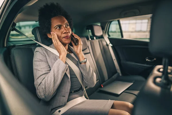 通勤中に車の後部座席に座っている間にスマートフォンで話して成功した黒人女性のショット — ストック写真