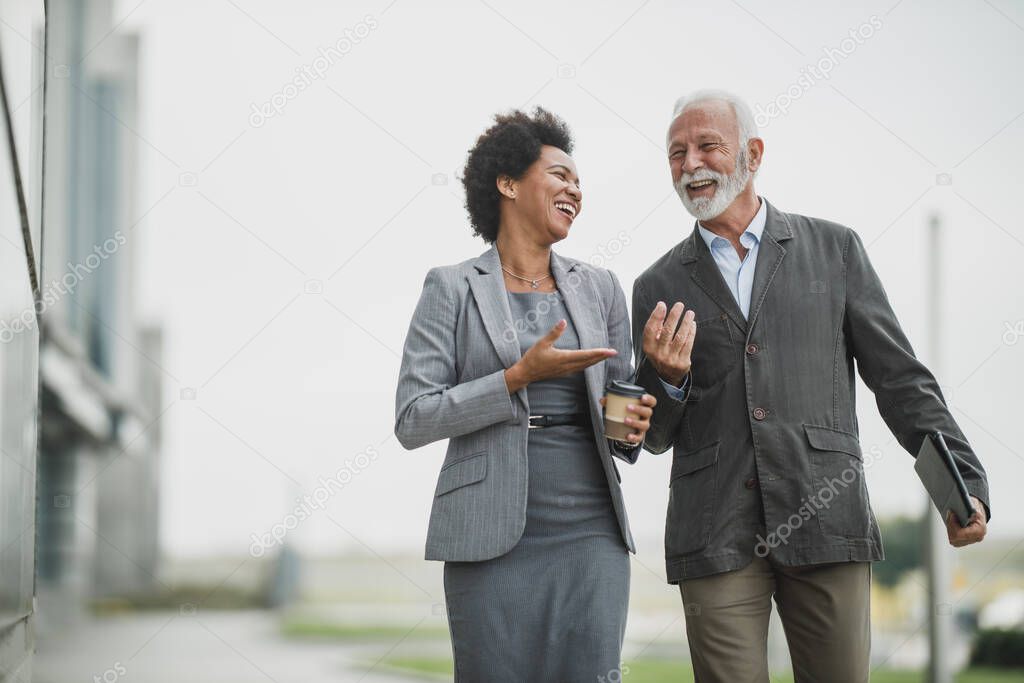 Shot of two successful multi-ethnic business people talking and having fun while walking during a coffee break outdoors.