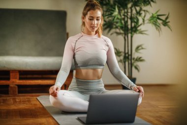 Gündüz evde egzersiz yaparken dizüstü bilgisayar kullanan çekici bir genç kadın..