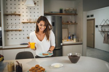 Genç bir kadın kahvaltısını yapıyor ve güneşli sabahını mutfakta geçiriyor..
