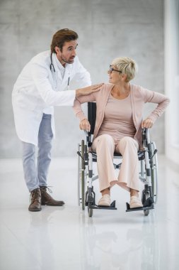 Tekerlekli sandalyedeki yaşlı bir kadına yardım eden genç bir doktor..