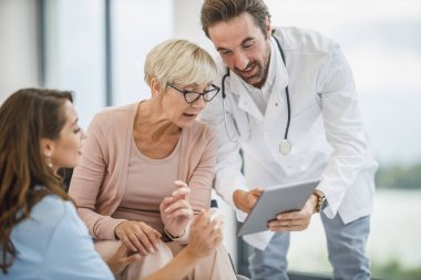 Başarılı doktor ve genç hemşire tekerlekli sandalyeye mahkum yaşlı kadın hastalarıyla konuşuyor..