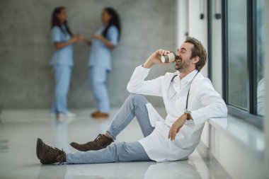 Başarılı bir doktorun, pencerenin yanında oturmuş hastane koridorunda kahve molası verirken mutlu görünmesi..