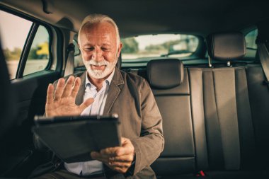 Başarılı bir kıdemli adamın iş seyahati sırasında arabanın arka koltuğunda otururken dijital tablet kullanması..