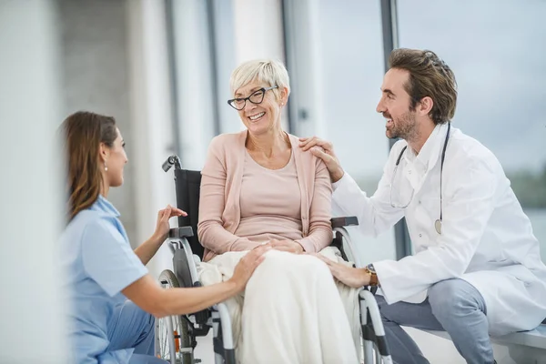 成功的医生和年轻护士与坐轮椅的老年女性病人交谈 — 图库照片