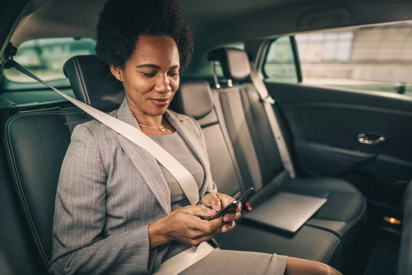 Strzał Odnoszącej Sukcesy Czarnej Bizneswoman Korzystającej Smartfona Siedzącej Tylnym Siedzeniu — Zdjęcie stockowe