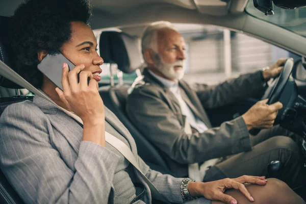 A successful black business woman talking on smartphone during her morning commute with her senior coworker.