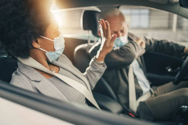 Covid 19パンデミックの間に車で移動する保護マスクを持つ2人の成功した多民族ビジネスの人々のショット — ストック写真