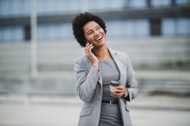Bir şirket binasının önünde kahve molası verirken akıllı bir telefonla konuşan neşeli bir siyahın portresi..