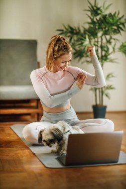 Evde egzersiz yaparken sağlıklı yaşam hakkındaki videosunu kaydetmek için dizüstü bilgisayar kullanan çekici genç bir kadın..