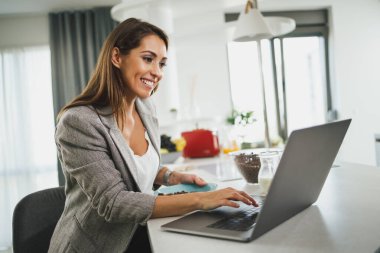 Dizüstü bilgisayarını kullanan ve işe gitmek için hazırlanan birden fazla işi olan genç bir iş kadını..