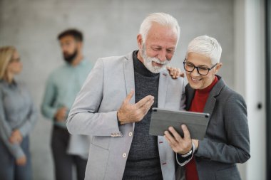 Modern bir ofiste buluşurken dijital tabletle video görüşmesi yapan iki kıdemli iş adamı..