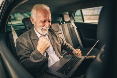 İş seyahati sırasında bir arabanın arka koltuğunda otururken başarılı bir kıdemli adamın dizüstü bilgisayar kullanması..