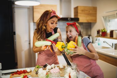 Gülümseyen annesine mutfakta taze sebze hazırlamasında yardım eden tatlı bir kız..