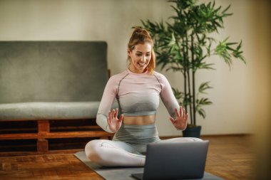 Evde egzersiz yaparken sağlıklı yaşam hakkındaki videosunu kaydetmek için dizüstü bilgisayar kullanan çekici genç bir kadın..