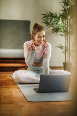 Evde egzersiz yaparken sağlıklı yaşam hakkındaki videosunu kaydetmek için dizüstü bilgisayar kullanan çekici genç bir kadın..