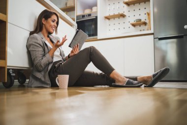 Gülümseyen kadın boş zamanlarını dijital tabletle geçirip evinde mutfakta yerde otururken video çekiyor..