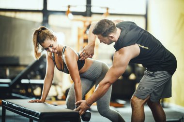 Çekici bir genç kadın spor salonundaki kişisel antrenörün kontrolünde bir halterle çalışıyor..