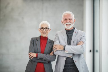 İki gülümseyen kıdemli iş adamının portresi modern bir ofiste kesişen ve kameraya bakan insanlar..