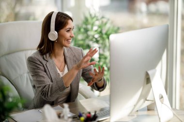 Kulaklıklı çekici bir iş kadını ve ev ofisinde internet konferansı düzenlemek için bilgisayar kullanıyor..