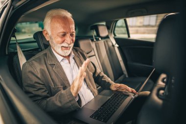 Başarılı bir kıdemli işadamının, sabah işe gidip gelirken bir arabanın arka koltuğunda otururken bilgisayarında video görüşmesi yaparken görüntüsü..