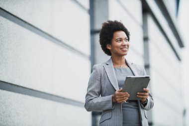 Şirket binasının önünde hızlı bir mola sırasında dijital tablet üzerinde çalışan başarılı bir zenci iş kadını portresi..