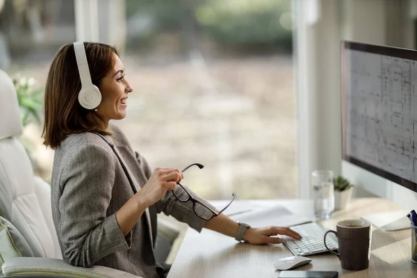 Neşeli bir iş kadını evinde kulaklıklarıyla tek başına oturuyor ve bilgisayarla çalışıyor..