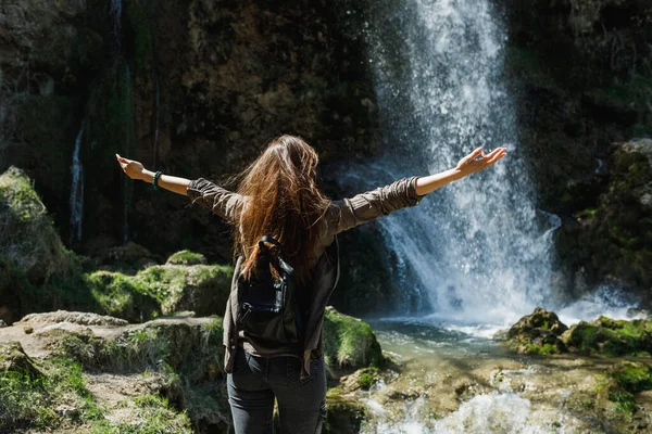 Rear view of a carefree young woman enjoying the view of the beautiful waterfall.