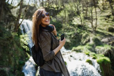 Neşeli genç bir kadın güzel şelalenin manzarasının tadını çıkarıyor..