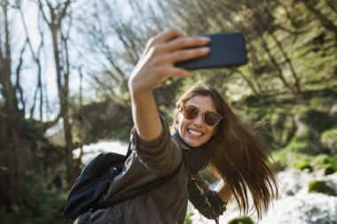 Tasasız genç bir kadın açık havada eğlenirken akıllı telefonuyla selfie çekiyor..