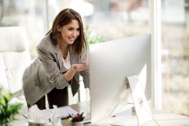 Ofisinde internet konferansı yapmak için bilgisayar kullanan çekici bir genç kadın..