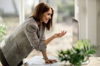 İnternette konferans vermek için bilgisayarını kullanan gülümseyen genç bir kadın..