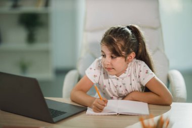 Evde online ders almak için bilgisayarını kullanan sevimli, çalışkan küçük bir kız..