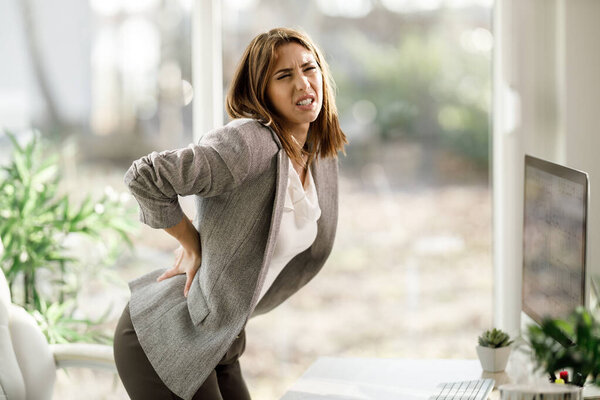 An attractive business woman experiencing back pain while working on computer in a modern office.
