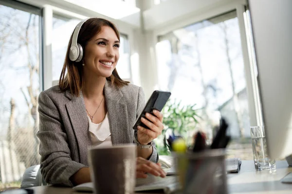 Leende Affärskvinna Med Hörlurar Som Använder Smartphone När Hon Arbetar — Stockfoto