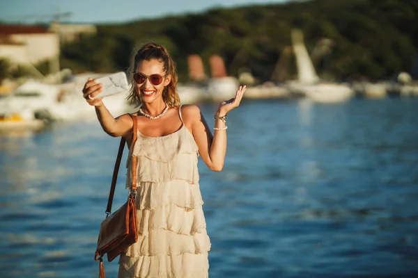 地中海の素晴らしい海辺を探索しながら 彼女のスマートフォンでビデオ通話を行う若い女性のショット — ストック写真