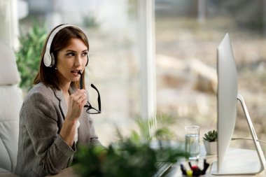 Çekici bir iş kadını evinde kulaklıklarla ve bilgisayarla tek başına oturuyor..