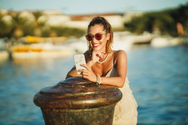 Akdeniz 'in harika sahil şeridini keşfederken akıllı telefonunu kullanan genç bir kadının fotoğrafı..