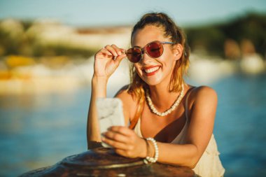 Akdeniz 'in harika sahil şeridini keşfederken akıllı telefonunu kullanan genç bir kadının fotoğrafı..