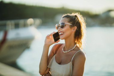 Akdeniz 'in muhteşem sahil şeridini keşfederken akıllı telefonuyla konuşan genç bir kadının fotoğrafı..