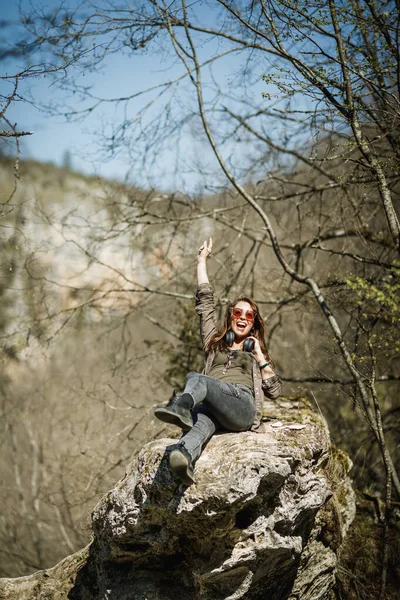 山の崖の上に座ってアウトドアを楽しんでいる陽気な若い女性 — ストック写真