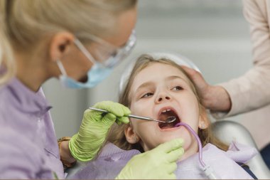 Dişçinin muayenehanesinde küçük tatlı bir kızın dişlerini muayene eden bir kadın diş hekimi..