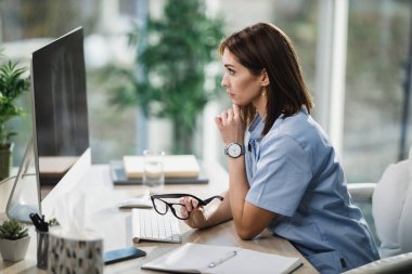 Çekici bir bayan doktor danışma odasında tek başına oturuyor ve bilgisayardaki röntgenlere bakıyor..