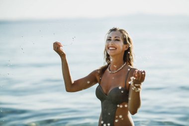 Güzel, gülümseyen bir kadın deniz suyunda eğleniyor ve tatilin tadını çıkarıyor..