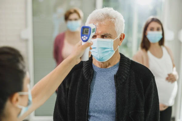 코로나 바이러스에 접종이 줄지어 기다리고 노인의 체온을 측정하는 간호사 — 스톡 사진