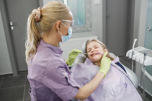 歯医者で歯医者の手術中にかわいい女の子の歯を調べる女性の歯科医 — ストック写真