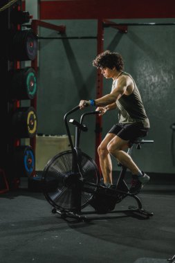 Genç kaslı bir adam spor salonunda motorlu taşıt eğitimi alıyor..