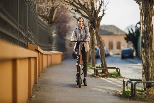 一位年轻的女商人骑着电动车在穿过城市的路上工作 — 图库照片