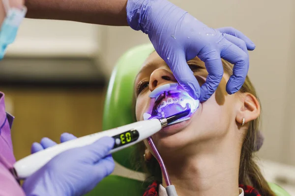 その少女は歯医者にいる 歯医者は赤外線ランプで歯にブレースをつけます — ストック写真