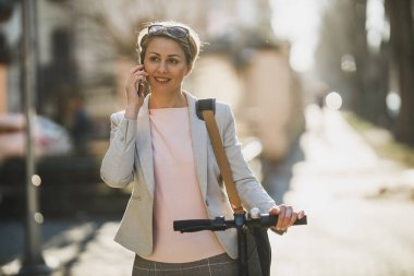Şehirde elektrikli scooterla gezerken akıllı telefon kullanan olgun bir iş kadını..